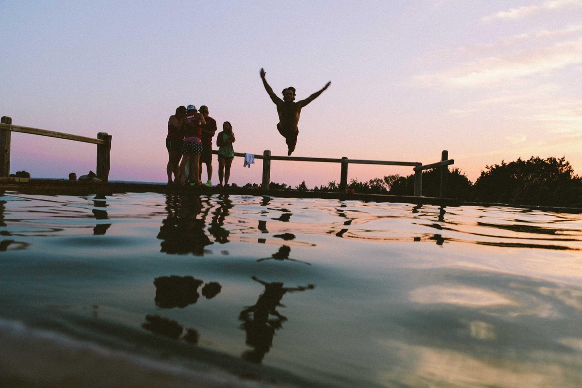 Friends jumping into a lake at sunset.